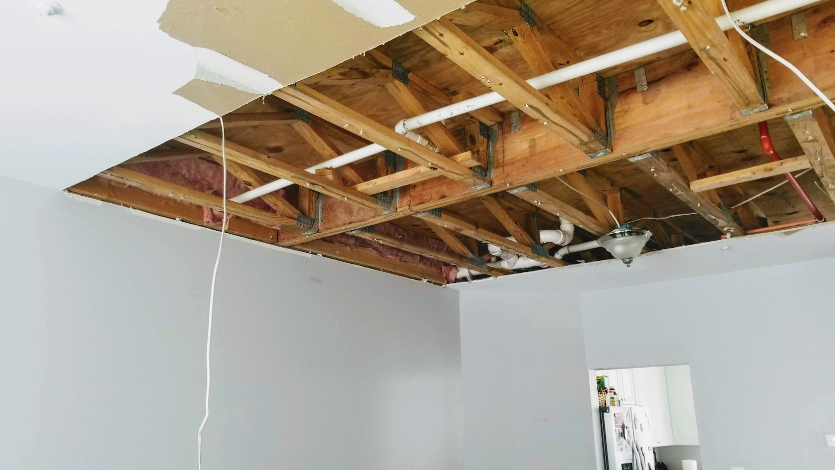 Large drywall ceiling cut for leak repair in a living room, showing a significant section needing replacement, with surrounding walls also requiring repainting.