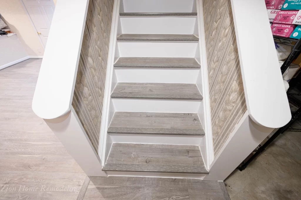 Modern basement stairs with white risers and vinyl plank flooring continuing from the kitchen, showing the replaced basement flooring in the background.